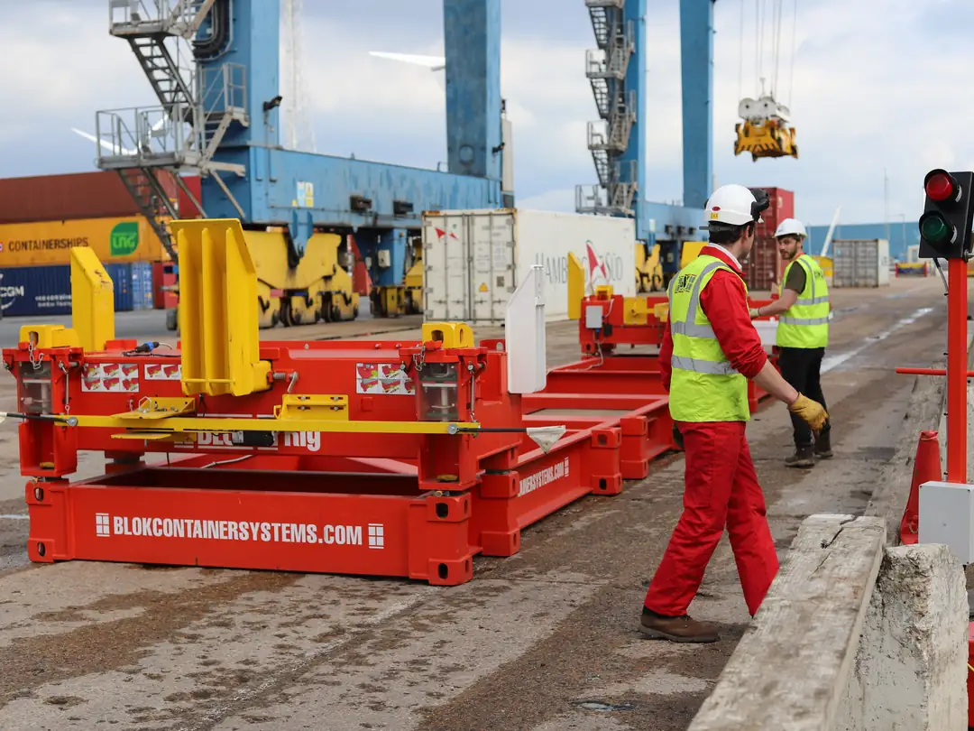 Engineers in hi-vis inspecting red container handling frames on a dockside