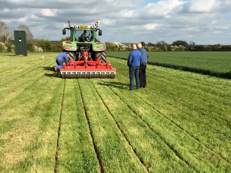 Tractor and mounted implement cutting slots in a grass field while engineers observe