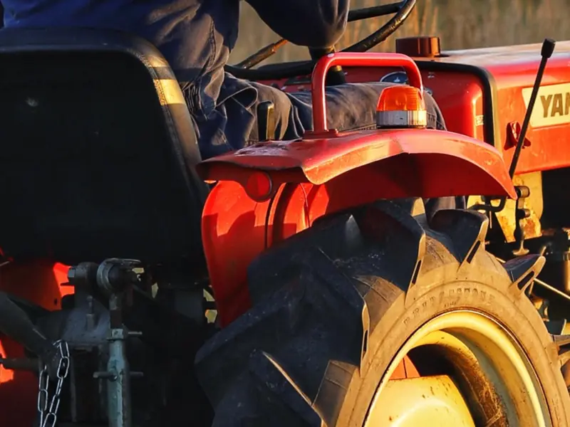 Driver on a red compact tractor in a field at dusk