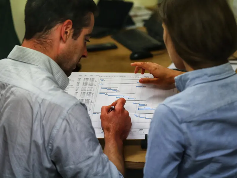 Two engineers reviewing a printed Gantt chart project plan at a desk